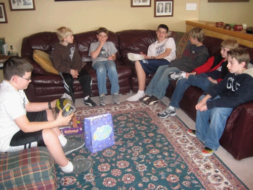 Clark's friends watching him open presents at his birthday party.