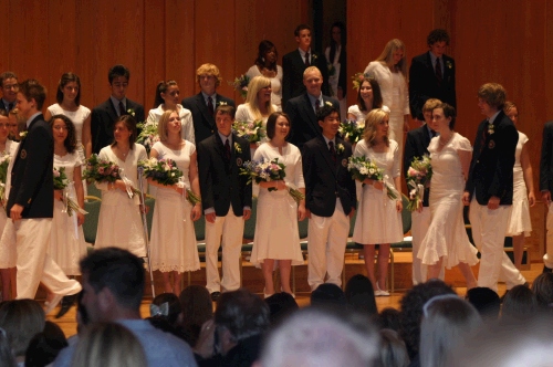 No caps and gowns -- the girls wear all white and the boys wear the school jacket and tie.  It looks quite cool actually.