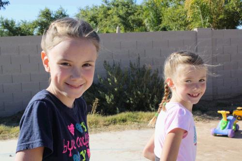 Julia and Karen with matching French braids having a great time playing on scooters outside in the back yard.